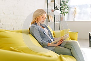 Young woman reading a book on cozy yellow couch