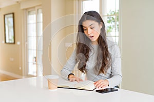 Young woman reading a book and drinking a coffe scared in shock with a surprise face, afraid and excited with fear expression