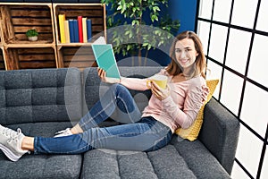 Young woman reading book and drinking coffee at home