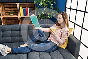 Young woman reading book and drinking coffee at home