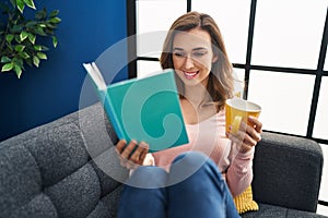 Young woman reading book and drinking coffee at home