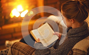 Young woman reading a book by the fireplace on a winter evenin