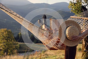 Young woman reading book in hammock outdoors at sunset