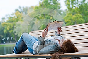 Young woman reading a book lying on the bench