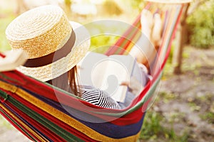 Young woman reading book while lying in comfortable hammock at green garden