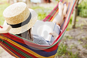 Young woman reading book while lying in comfortable hammock at green garden