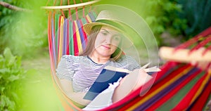 Young woman reading book while lying in comfortable hammock at green garden