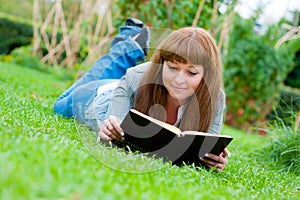 Young woman reading a book lying on the grass