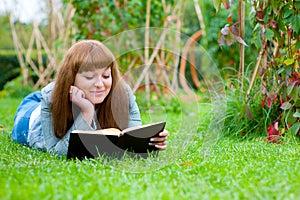 Young woman reading a book lying on the grass