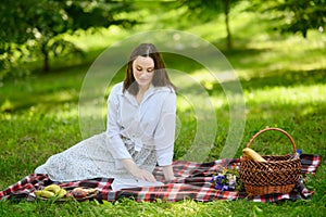 Young woman reading a book on an outdoor picnic, sitting on a blanket in the park, relaxing in the summer.