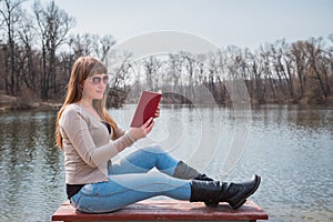 Young woman reading the book outdoor in sunglasses, daily lifestyle, river on the background, spring, sunny day
