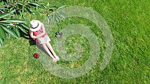 Young woman reading book in park near bike. Student girl relaxing outdoors sitting on grass with book and headphones