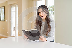 Young woman reading a book scared in shock with a surprise face, afraid and excited with fear expression