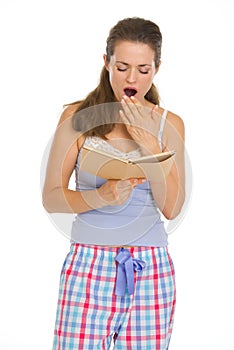 Young woman reading book before sleep and yawing photo