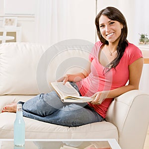 Young woman reading book on sofa at home