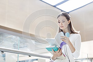 Young woman reading book while standing by railing at university