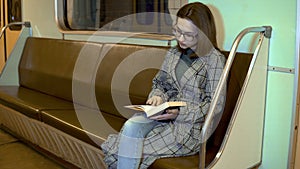 A young woman is reading a book in a subway train. Old subway car