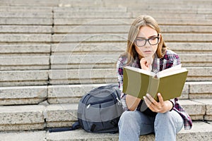 Young woman reading book on university stairs