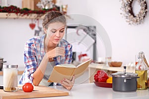 Young woman reading cookbook in the kitchen, looking for recipe