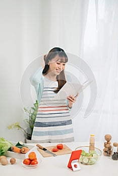 Young woman reading cookbook in the kitchen, looking for recipe