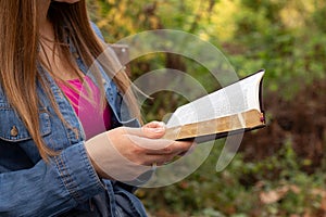 Young woman reading a holy bible book in the park, close up