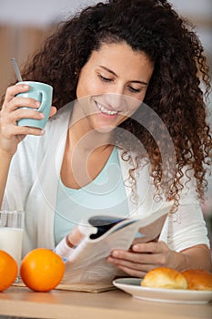 Young woman reading news while having breakfast