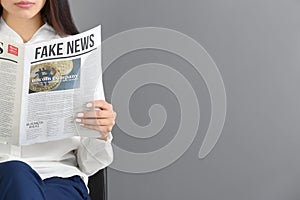 Young woman reading newspaper against grey background