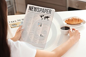 Young woman reading newspaper while drinking coffee in kitchen