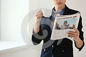 Young woman reading newspaper while drinking coffee in office