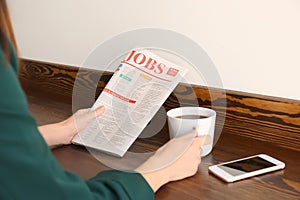 Young woman reading newspaper while drinking coffee at table indoors