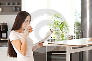 Young woman reading newspaper while drinking juice in kitchen