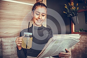 Young woman reading newspaper and drinking lemonade