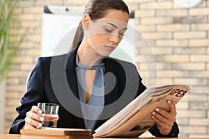 Young woman reading newspaper while drinking water in office