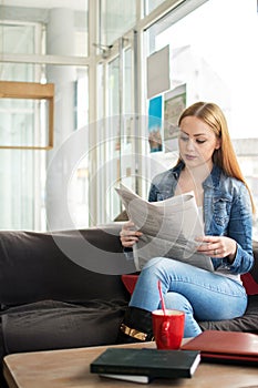 Young woman reading newspaper and having coffee break