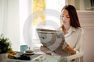 Young woman reading newspaper while having morning coffee at home