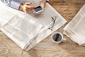 Young woman reading newspaper and holding phone