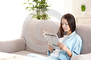 Young woman reading newspaper indoors