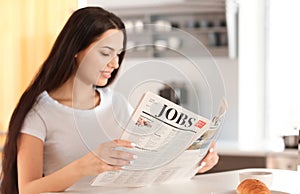 Young woman reading newspaper in kitchen