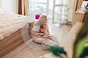 Young woman reading to her baby son at home. Mother and kid sitting on floor with book