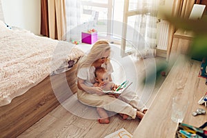 Young woman reading to her baby son at home. Mother and kid sitting on floor with book. Mother`s day