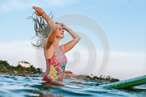 young woman readjusting wet hair while sitting on surfing board