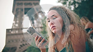 Young woman reads a message on her smartphone at the Eiffel Tower in Paris, France