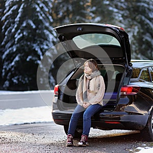 Young woman ready to go on vacations and relaxing in the opened trunk of a car before a road trip