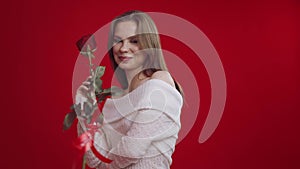 Young woman receives rose and becomes happy on red background