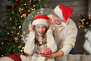 Young woman receiving Christmas gift from her boyfriend at home photo