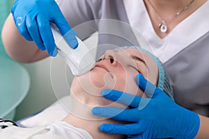 Young woman receiving electric galvanic anti-aging face spa massage at beauty salon