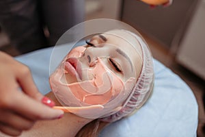 Young woman receiving facial beauty treatment in Beauty salon, applying of Alginate Peel-Off Powder facial Mask. Half of the face