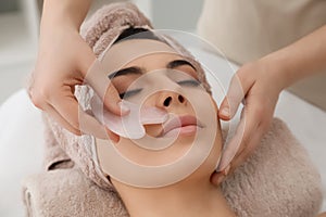 Young woman receiving facial massage with gua sha tool in beauty salon photo