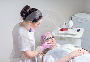 Young woman receiving laser treatment in cosmetology clinic. Eyes covered with protection glasses