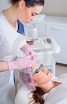 Young woman receiving laser treatment in cosmetology clinic. Eyes covered with protection glasses